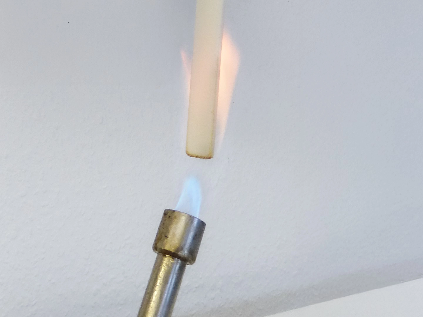 Ein eingeschalteter Gasbrenner der ein Kunststoff entzündet. Blaue und gelbe Flammen.