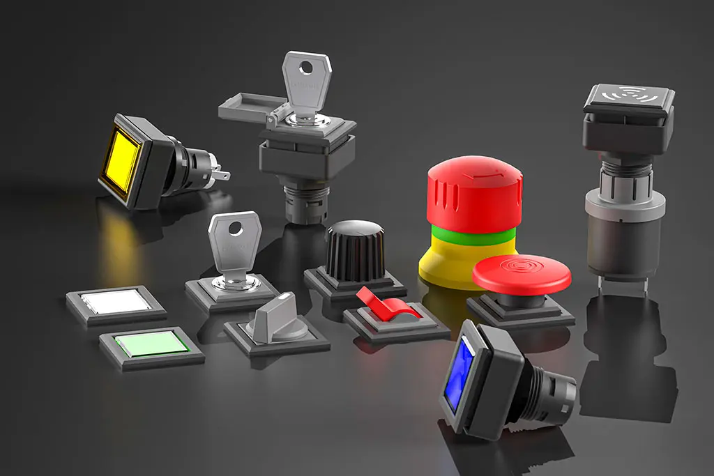 Not-Halt-Taster, quadratische Drucktasten, Schlüsselschalter und Wahlschalter auf einer schwarz-spiegelnden Oberfläche. Manche Taster liegen, andere stehen.